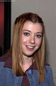 a woman with long red hair and blue shirt smiling at the camera while standing in front of a wall