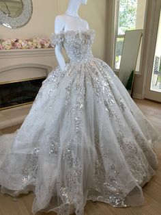 a white wedding dress with silver sequins is on display in front of a fireplace