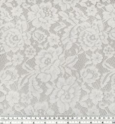 a white lace fabric with flowers and leaves on the side, in front of a ruler