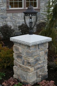 a lamp on top of a stone pillar in front of a window and shrubbery