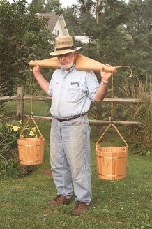 a man is holding two buckets and a wooden board on his shoulders while standing in the grass