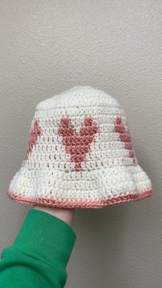 someone is holding up a crocheted white and pink hat with hearts on it