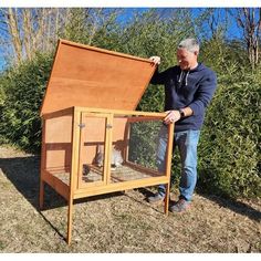 a man holding up a small cage with a cat in it on top of grass