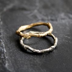 two gold rings sitting on top of a stone slab, with one ring in the shape of a twig