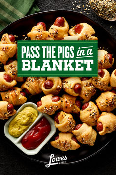 pigs in a blanket with ketchup and mustard on a black plate next to condiments