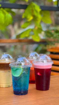 four different colored drinks sitting on top of a wooden table