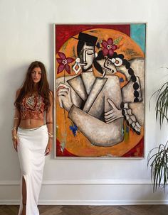 a woman standing in front of a painting on the wall next to a potted plant