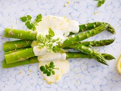 asparagus with sour cream and parsley on a blue plate next to a slice of lemon