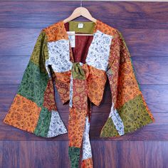 Add a dash of bohemian charm to your wardrobe with this colorful paisley print bell sleeve patchwork top. Perfect for festival lovers and free-spirited souls alike. Design & Print: Paisley Print: Features a whimsical mix of paisley prints in earthy tones. Colorful Patchwork: Crafted from a vibrant combination of warm colors including oranges, greens, and browns. Bell Sleeves & Crop Length: Bell Sleeves: Wide, flowing sleeves add a dramatic and stylish flair. Crop Length: Finished with a flattering tie-front closure at the waist. Material & Fit: Material: Made from lightweight and breathable cotton for comfort. Fit: Relaxed fit makes it ideal for layering over a tank top or bikini. Boho Style: Perfect for music festivals, beach outings, or casual everyday wear. Embodies the free-spirited hi Bohemian Patchwork Blouse For Spring, Bohemian Spring Blouse With Patchwork, Bohemian Spring Patchwork Blouse, Spring Bohemian Patchwork Blouse, Bohemian Patchwork Blouse For Festival, Fall Festival Bohemian Peasant Top, Hippie Long Sleeve Top With Boho Collar, Multicolor Patchwork Blouse For Festival, Bohemian Long Sleeve Tops With Boho Collar