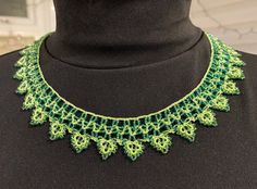 a green and yellow crochet necklace on a black mannequin neckline