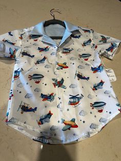 Classy crisp Airplane-Themed button-down shirt for either boys or girls.  What could be better than a nice, button-down shirt?  This version is made up of 100% white cotton printed with airplanes, clouds, helicopters, and stars  The inside yoke is made of 100% cotton blue and white striped fabric.  The shirt-tails are rounded for a more relaxed look. Available in a child's size 8 and Baby size 18-24 months.  Matching striped shorts available in size 18-24 elsewhere in this shop. Collared Shirt For School In Summer, Collared Summer Shirt For School, Cute White Button Shirt, Cute White Button-up Shirt, School Cotton Shirt With Button Closure, White Printed Button-up Short Sleeve Shirt, Short Sleeve Shirt With Button Closure For Playtime, Playful Collared Cotton Shirt, Summer School Shirt With Buttons