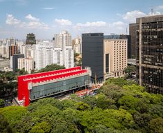 an aerial view of a city with tall buildings and trees in the foreground, on a sunny day