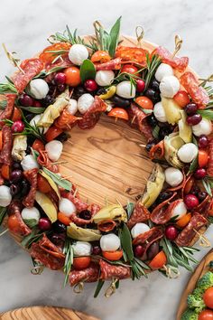 a wreath made out of vegetables and meats on a marble counter top next to wooden cutting board