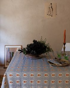 a table topped with a bowl filled with green plants next to an orange lit candle