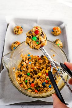 a person holding a spoon over a bowl filled with cereal and m & m cookies