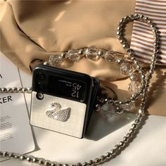 a cell phone with a chain attached to it sitting on top of a bed next to a purse