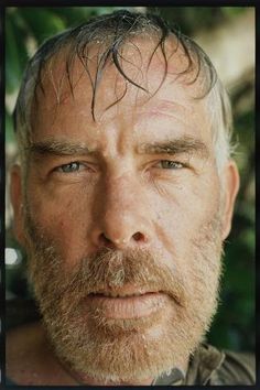 a close up of a person with a beard and wearing a brown shirt looking at the camera