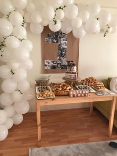 a table topped with lots of white balloons and pastries next to a wall filled with pictures