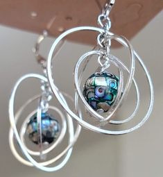 These earrings are made with a mosiac abalone stone and orbiting hoops. These unique earrings have lovely movement and are subtle yet eye catching. With dreamy swirls of blue, green, and purple, these earrings just gorgeous.  These earrings are 2inches from top to bottom and 1 1/4 inches wide.  Lever Back closures are made of Sterling Silver. Hoops themselves are made of nickel free alloy. Iridescent Dangle Earrings Nickel Free, Fusion Style Metal Earrings For Gift, Iridescent Drop Earrings For Jewelry Making, Silver Fusion Style Wire Wrapped Earrings, Wire Wrapped Fusion Earrings For Gift, Fusion Style Wire Wrapped Earrings For Gift, Nickel Free Fusion Drop Earrings, Iridescent Ear Wire Earrings For Gift, Nickel-free Fusion Style Drop Earrings