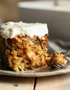 a piece of carrot cake with cream cheese frosting on a plate next to a fork