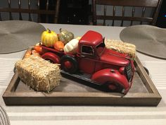 a red truck with hay bales and pumpkins on it sitting on top of a wooden tray