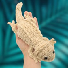 a hand holding a small crocheted gecko toy in it's palm