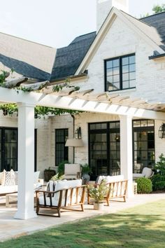 an outdoor patio with white pergoline and wooden furniture on the grass near a house