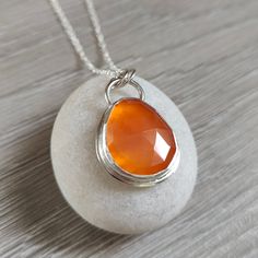 A beautiful vibrant orange teardrop shaped stone set in silver.  This piece of Carnelian is 10.64 carat weight and has been rose cut to catch the light which really emphasizes it's beautiful colour.  The stone is set in a Fine Silver bezel and sits on 0.8mm Sterling Silver sheet.  The top loop is made from 1.3mm Sterling Silver wire and the two bail loops are made from 1mm Sterling Silver wire. The pendant including the bail loops measures 32mm x 19.5mm.  The stone measures 20.3mm x 16.5mm.  The Orange Briolette Jewelry For Gift, Orange Gemstone Drop Jewelry, Orange Drop Gemstone Jewelry, Pear-shaped Orange Jewelry Gift, Orange Pear-shaped Jewelry For Gifts, Orange Pear-shaped Jewelry, Silver Teardrop Carnelian Jewelry, Silver Carnelian Teardrop Jewelry, Carnelian Gemstone Drop Jewelry