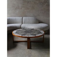 a white couch sitting next to a wooden table on top of a cement floor in front of a concrete wall