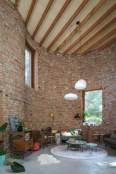 a living room filled with furniture and large windows next to a brick wall covered in wood beams