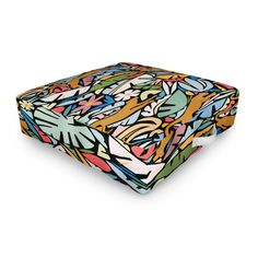 a square cushion with colorful flowers and leaves on the front, sitting on a white surface