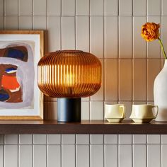 an orange flower sitting on top of a shelf next to two cups and a vase