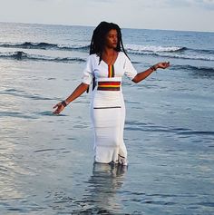 a woman is standing in the water at the beach with her arms out and she's wearing a white dress