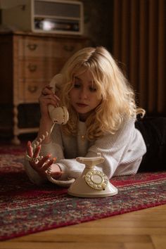 a woman laying on the floor while talking on an old fashioned phone with her hands