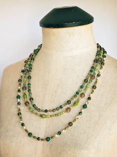 The captivating "Golden Green" necklace is a stunning combination of various beads in an array of shapes, sizes, and colors. This necklace features an eclectic mix of materials including glass, Malachite, Moss Tree Agate, Frosted Yellow Turquoise, Citrine, Purple Dyed Quartz, Diopside, Green Jade, textured and smooth golden metal, and acrylic. Each strand of this necklace is carefully crafted to showcase the unique beauty of its components adorned with a lush assortment of beads in vibrant shade Green Beaded Long Crystal Necklace, Long Green Beaded Crystal Necklace, Elegant Green Beaded Long Crystal Necklace, Bohemian Green Crystal Necklace With Colorful Beads, Green Bohemian Crystal Necklaces With Round Beads, Multi-strand Green Large Beads, Bohemian Green Crystal Necklaces With Round Beads, Bohemian Green Crystal Round Beads Necklace, Green Oval Beaded Chain Jewelry