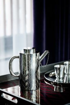 a silver coffee pot sitting on top of a table next to cups and saucers