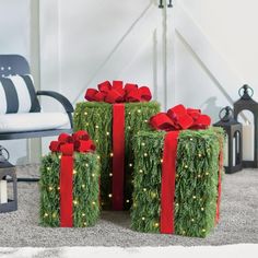 three presents wrapped in green grass with red bows and lights are sitting on the floor