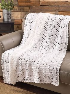 a white crocheted blanket sitting on top of a couch next to a table