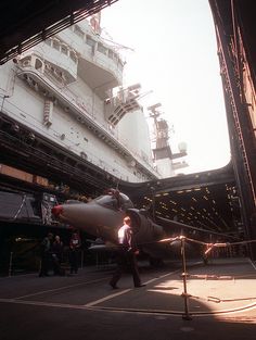 a fighter jet sitting on top of an airport tarmac next to a large ship