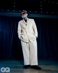 an old man in a suit and hat standing on stage with his hands in his pockets