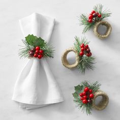 three napkin rings decorated with holly and red berries on top of a white table cloth