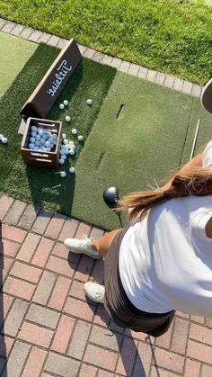 a woman sitting on the ground next to a box of golf balls and tees