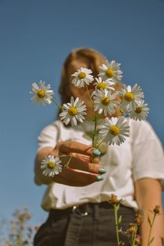 a woman is holding daisies in her hands