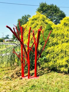 three red sculptures in the middle of a grassy area with trees and bushes behind them