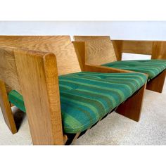 a wooden bench with green fabric on it's seat and back rests against a white wall