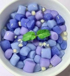 a bowl filled with blue and purple marshmallows next to a green leaf