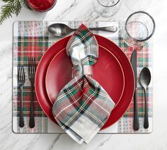 a place setting with red plates, silverware and plaid napkins