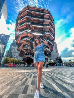 a woman standing on the street in front of a tall building with many floors and windows