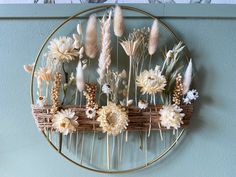 an arrangement of dried flowers on a circular metal frame hanging on the wall above a bed