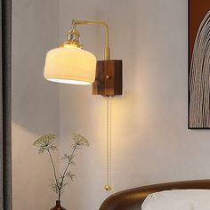 a wall light that is on the side of a wall next to a bed and vase with flowers in it